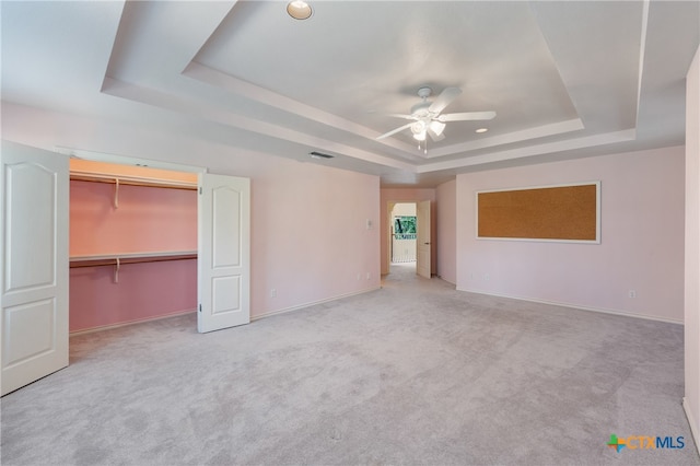 unfurnished bedroom with a closet, light carpet, ceiling fan, and a raised ceiling