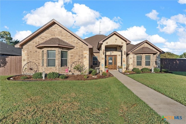 french provincial home with fence, brick siding, and a front yard