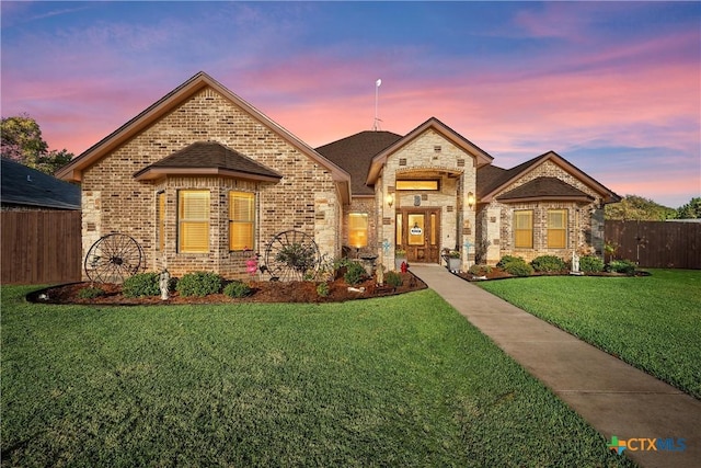 french country inspired facade featuring brick siding, fence, and a yard