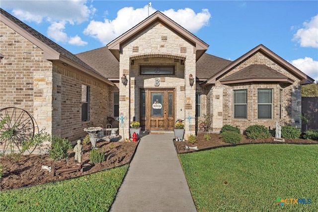 property entrance featuring brick siding, a lawn, and a shingled roof