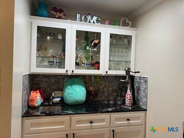 bar featuring sink, crown molding, tasteful backsplash, dark stone counters, and white cabinets