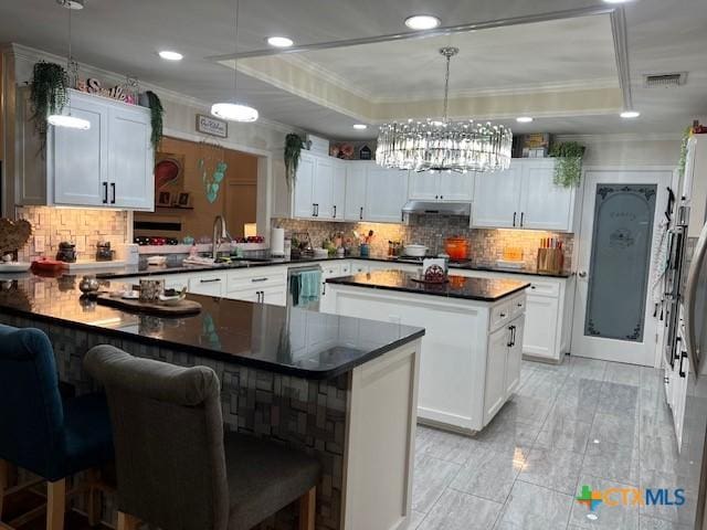 kitchen with a raised ceiling, white cabinetry, a kitchen island, and pendant lighting