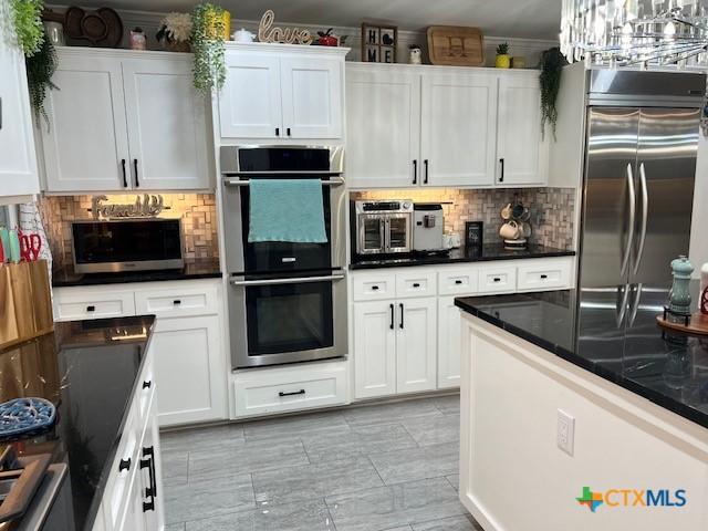 kitchen featuring white cabinetry, appliances with stainless steel finishes, hanging light fixtures, and tasteful backsplash