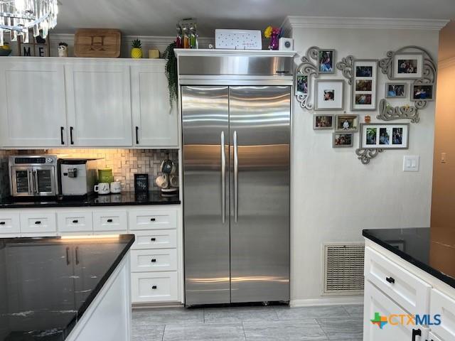 kitchen featuring white cabinetry, stainless steel built in refrigerator, crown molding, and decorative backsplash