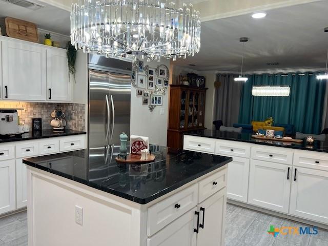 kitchen with built in fridge, a kitchen island, white cabinets, backsplash, and hanging light fixtures