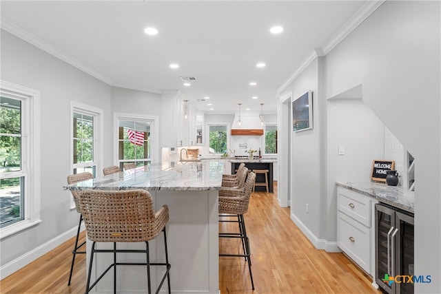 kitchen with light hardwood / wood-style floors, beverage cooler, crown molding, a breakfast bar, and white cabinetry