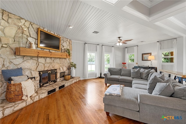 living room featuring ceiling fan, wood-type flooring, a stone fireplace, and ornamental molding