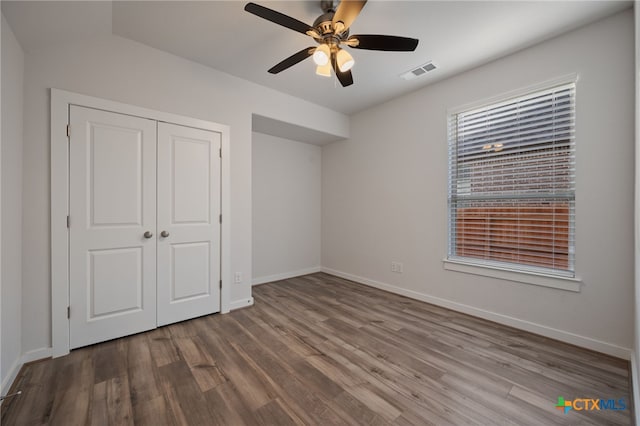 unfurnished bedroom with wood finished floors, visible vents, a closet, and baseboards