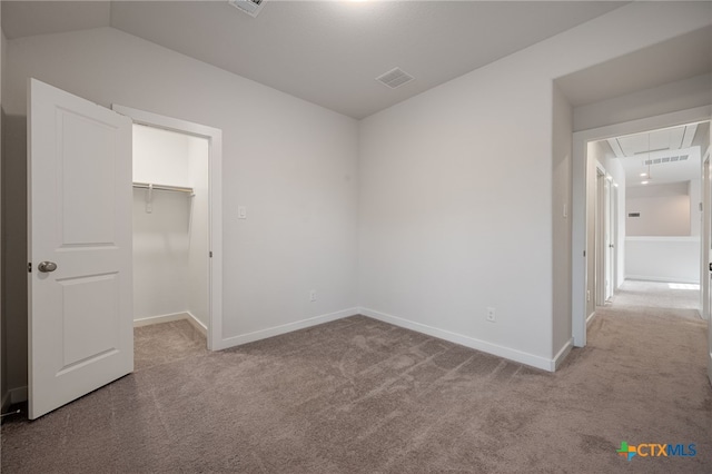 unfurnished bedroom with a walk in closet, attic access, visible vents, and carpet floors