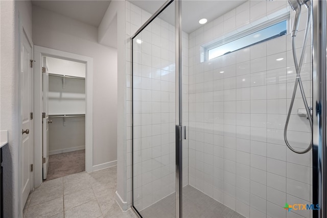 bathroom featuring tile patterned flooring, a shower stall, a spacious closet, and baseboards