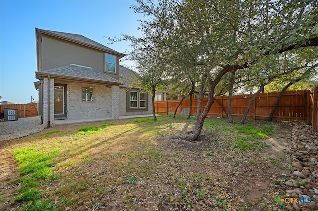 rear view of property with brick siding, a shingled roof, a yard, a fenced backyard, and a patio