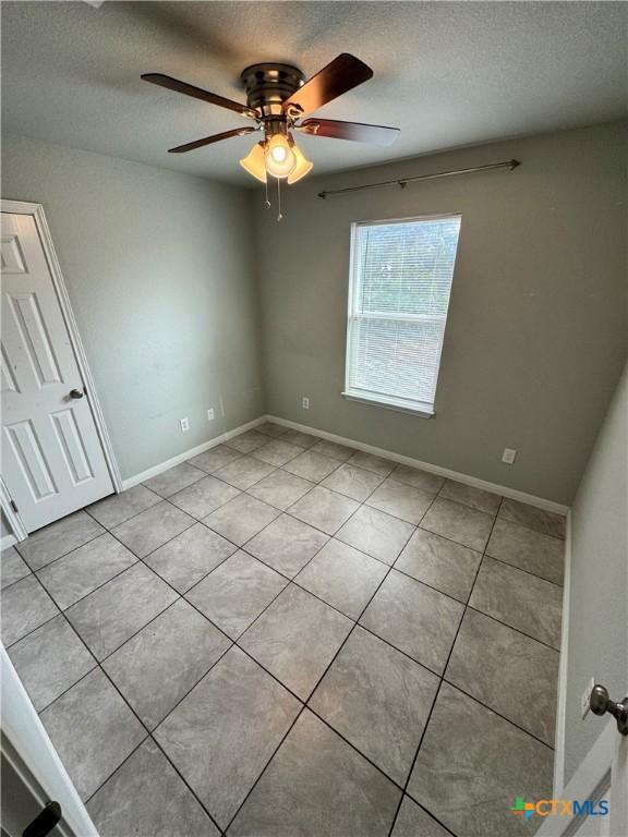 spare room featuring ceiling fan, light tile patterned floors, and a textured ceiling