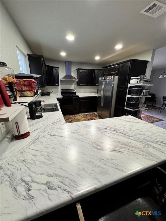 kitchen featuring wall chimney exhaust hood, black electric range oven, sink, and stainless steel refrigerator