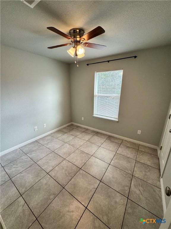 empty room with light tile patterned floors, a textured ceiling, and ceiling fan