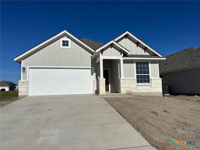 craftsman-style house with driveway, board and batten siding, stone siding, an attached garage, and central AC