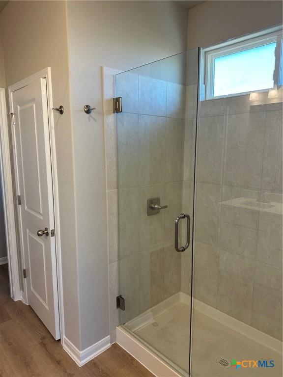 full bathroom featuring a stall shower, baseboards, and wood finished floors