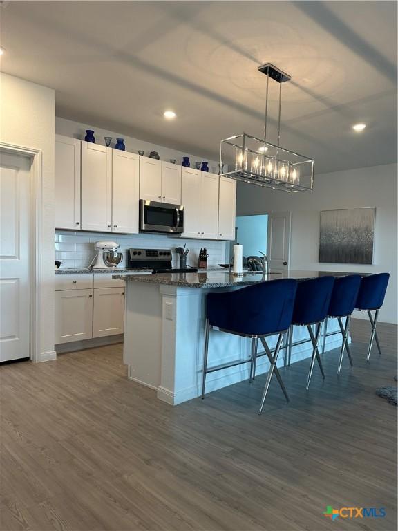 kitchen featuring pendant lighting, white cabinets, a kitchen bar, dark stone counters, and stainless steel appliances