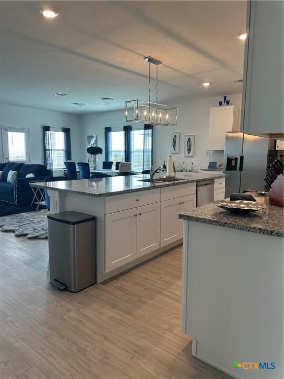 kitchen featuring appliances with stainless steel finishes, sink, white cabinets, hanging light fixtures, and a kitchen island with sink