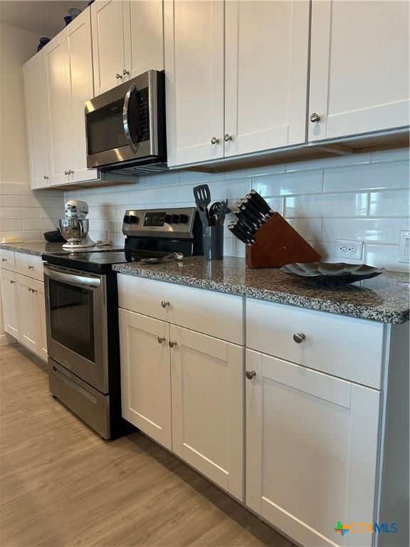 kitchen with tasteful backsplash, appliances with stainless steel finishes, white cabinets, and light wood-type flooring