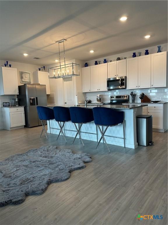 kitchen with pendant lighting, white cabinetry, a kitchen bar, stainless steel appliances, and a center island with sink