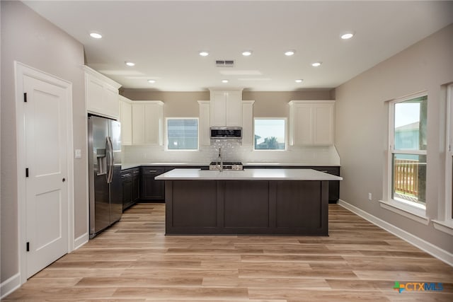 kitchen with light hardwood / wood-style flooring, decorative backsplash, a kitchen island with sink, and stainless steel appliances