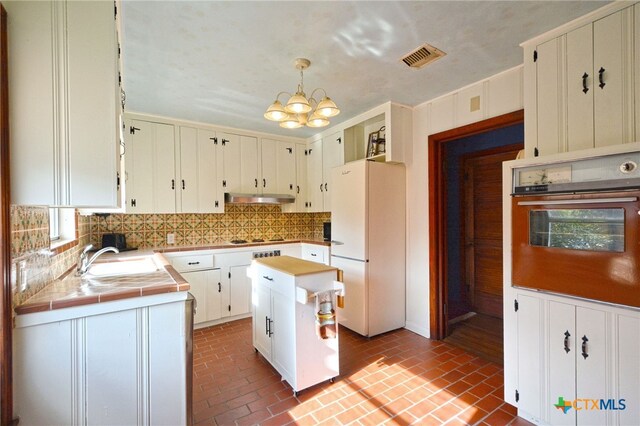 929 E Cedar St, Seguin, TX 78155 - kitchen with freestanding refrigerator, oven, brick floors, under cabinet range hood, and a chandelier