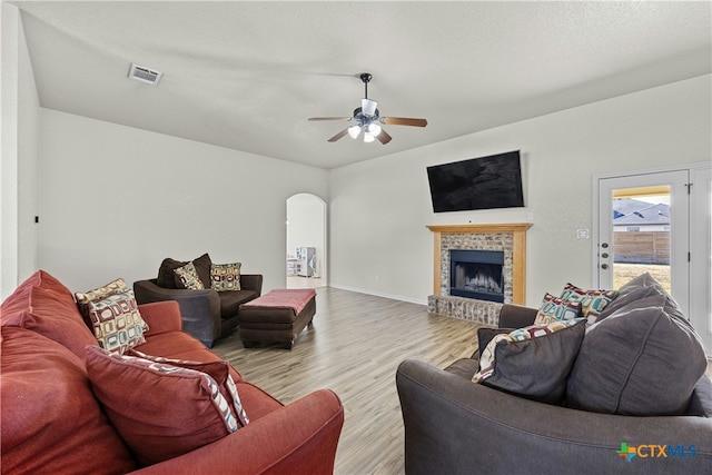 living room featuring ceiling fan, light hardwood / wood-style floors, a textured ceiling, and a brick fireplace