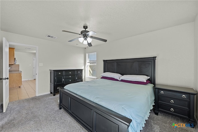 bedroom featuring a textured ceiling, light colored carpet, and ceiling fan