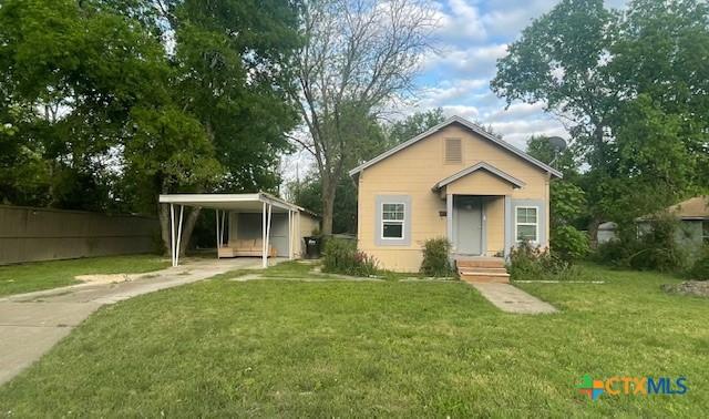 bungalow-style home with concrete driveway, a carport, a front yard, and fence