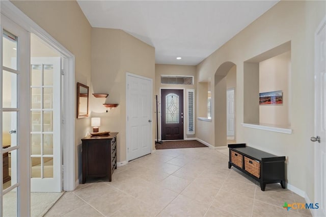 entrance foyer featuring light tile patterned flooring, arched walkways, french doors, and baseboards