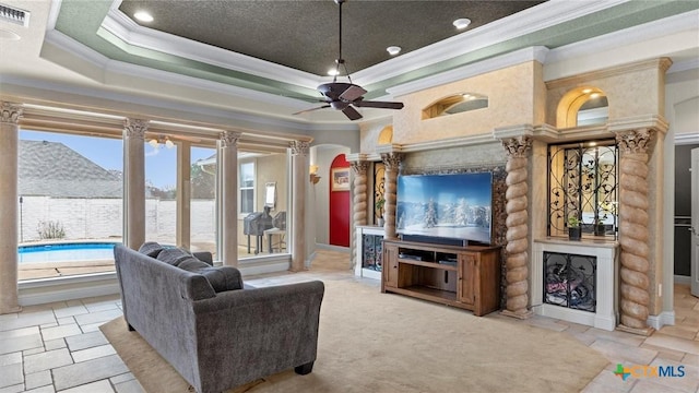 living room featuring decorative columns, crown molding, a raised ceiling, and ceiling fan