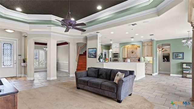 tiled living room with ornamental molding, ceiling fan with notable chandelier, and a tray ceiling