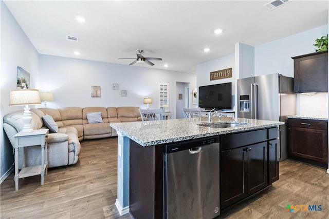 kitchen with a center island with sink, visible vents, a sink, light wood-style floors, and appliances with stainless steel finishes