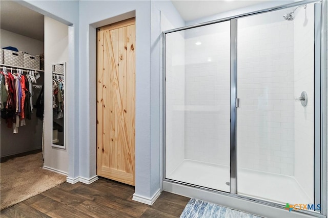 full bath featuring a spacious closet, a stall shower, and wood finished floors