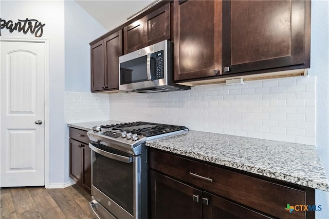 kitchen featuring light stone counters, appliances with stainless steel finishes, decorative backsplash, dark brown cabinets, and dark wood-style flooring