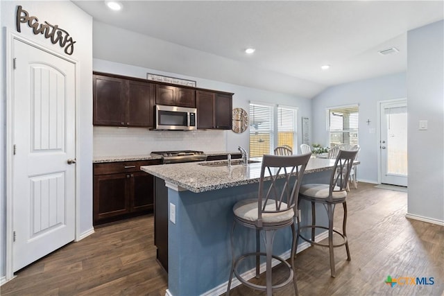 kitchen with stainless steel microwave, dark brown cabinets, a kitchen breakfast bar, and dark wood-type flooring