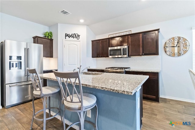 kitchen featuring visible vents, dark brown cabinetry, decorative backsplash, appliances with stainless steel finishes, and a sink