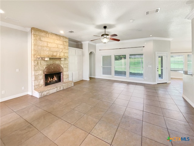 unfurnished living room with a textured ceiling, ceiling fan, crown molding, a stone fireplace, and light tile patterned flooring