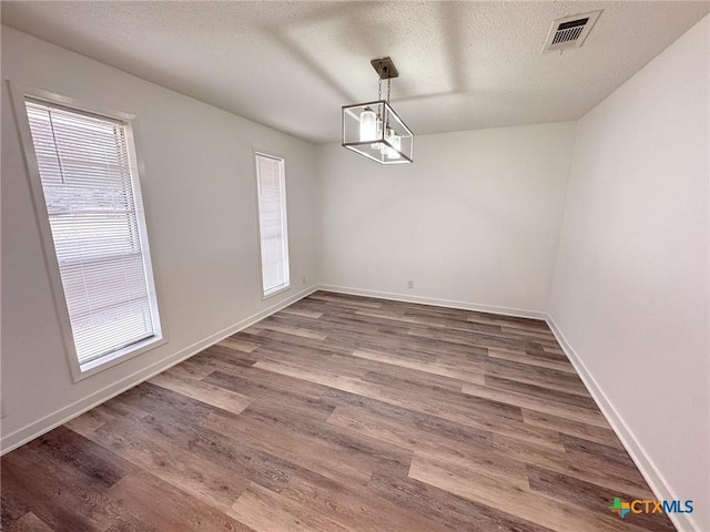 unfurnished dining area featuring a textured ceiling, a chandelier, and dark hardwood / wood-style floors