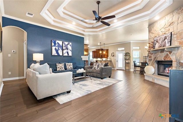 living room with crown molding, dark hardwood / wood-style floors, a tray ceiling, ceiling fan, and a fireplace