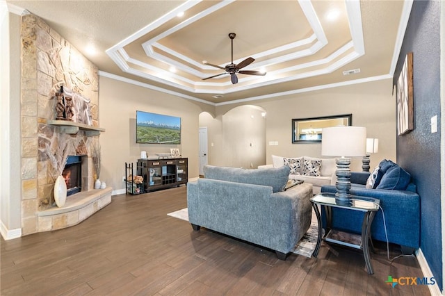 living room with a stone fireplace, crown molding, dark hardwood / wood-style floors, a raised ceiling, and ceiling fan