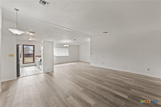 unfurnished living room featuring an inviting chandelier and light hardwood / wood-style flooring