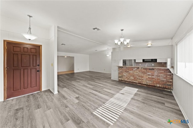 foyer entrance with an inviting chandelier, vaulted ceiling, and light hardwood / wood-style flooring