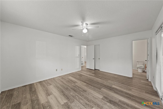 unfurnished bedroom featuring ceiling fan, ensuite bathroom, hardwood / wood-style floors, and a textured ceiling