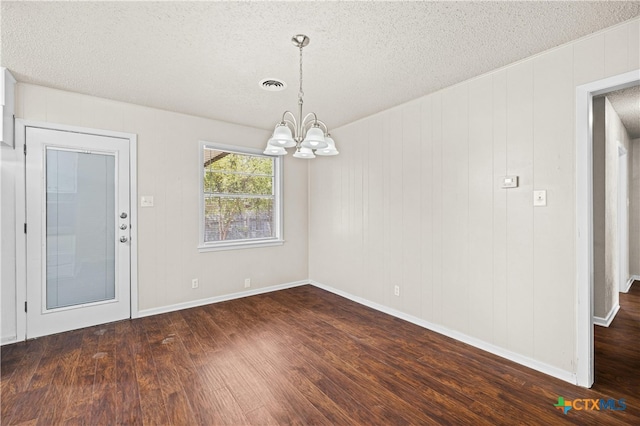 unfurnished dining area with wooden walls, dark wood-type flooring, a textured ceiling, and a notable chandelier