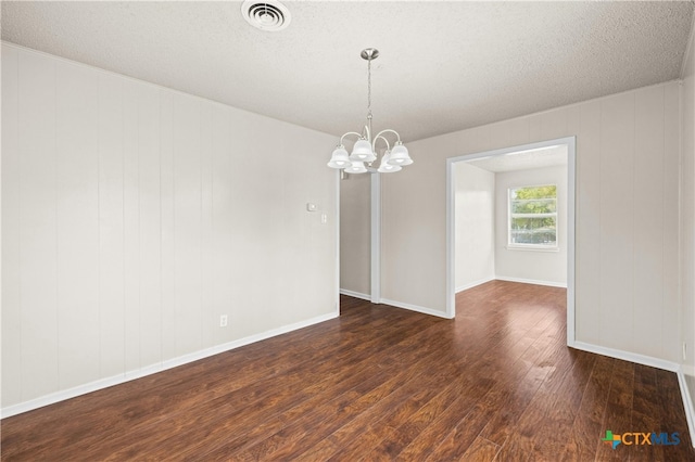 spare room featuring wooden walls, dark wood-type flooring, a textured ceiling, and a notable chandelier