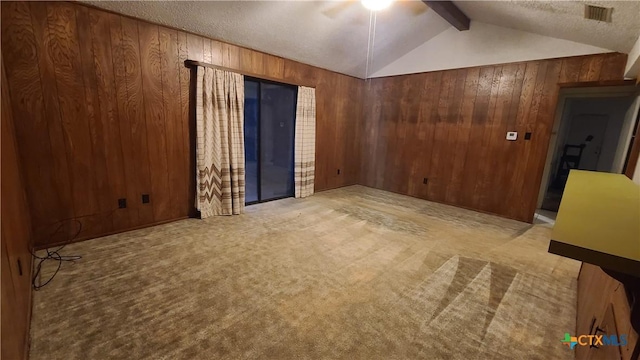 carpeted spare room with lofted ceiling with beams, wood walls, a textured ceiling, and ceiling fan