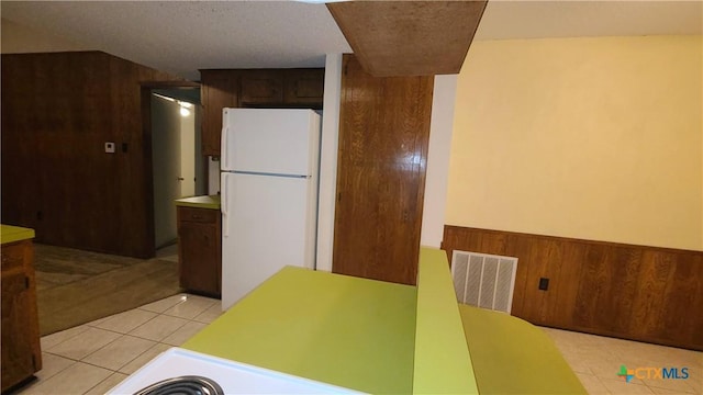 kitchen with wood walls, white refrigerator, dark brown cabinetry, and light tile patterned floors