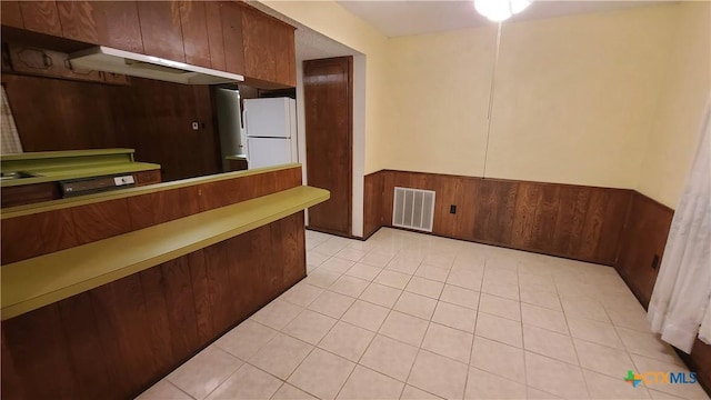 kitchen featuring wooden walls, white fridge, and light tile patterned floors