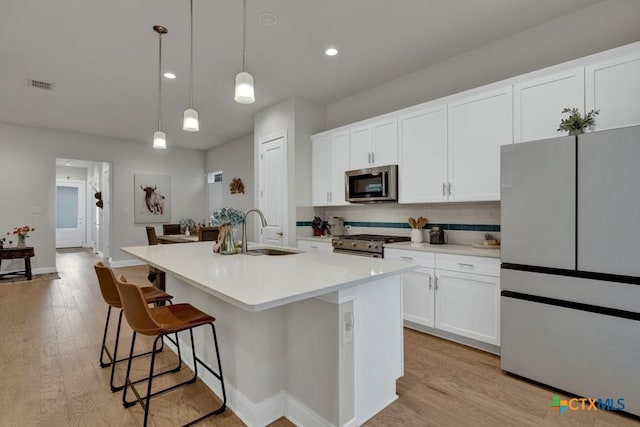 kitchen featuring backsplash, visible vents, appliances with stainless steel finishes, a sink, and an island with sink